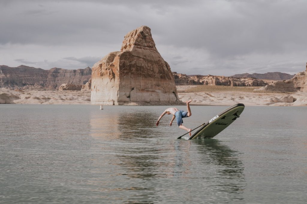Paddle Boarder Falling Into Water in Front of Rock Formation